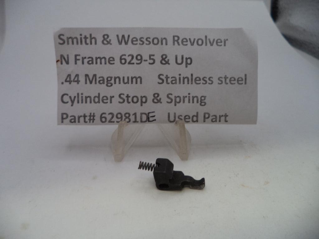 A small black metal cylinder stop and spring part for a Smith & Wesson revolver, displayed on a clear plastic stand in front of a printed label card.