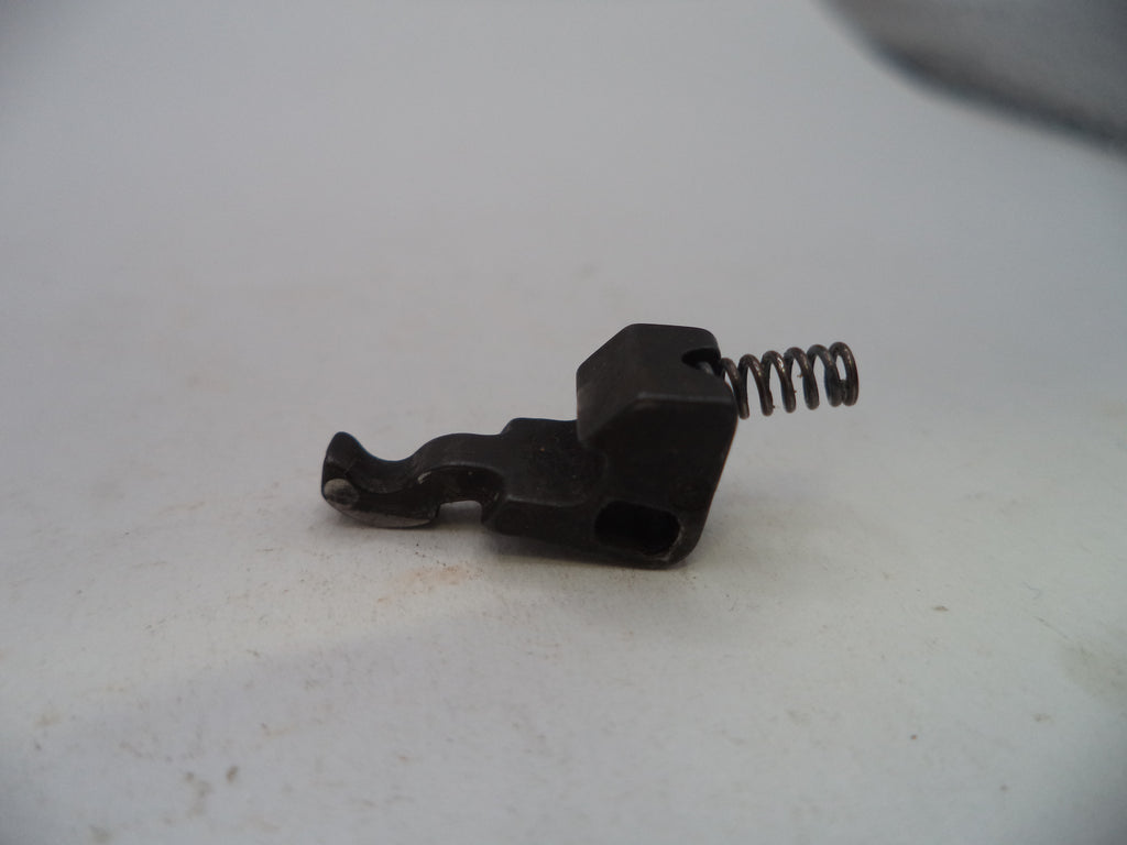 A small black metal mechanical component with a coiled spring, photographed on a plain off-white surface.