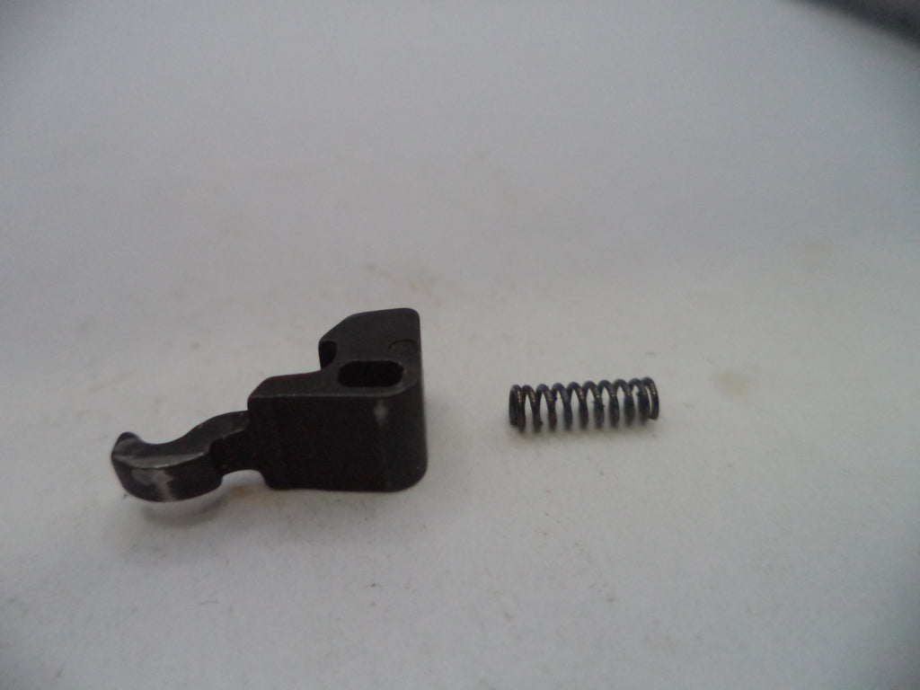 A small black metal mechanical component with a coiled metal spring next to it, photographed on a plain light gray surface.