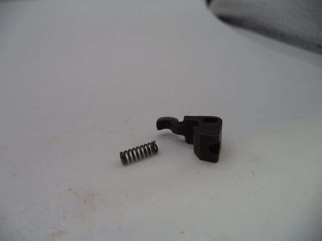 A small black plastic mechanical switch component with a separate metal coil spring, placed on a light gray surface.
