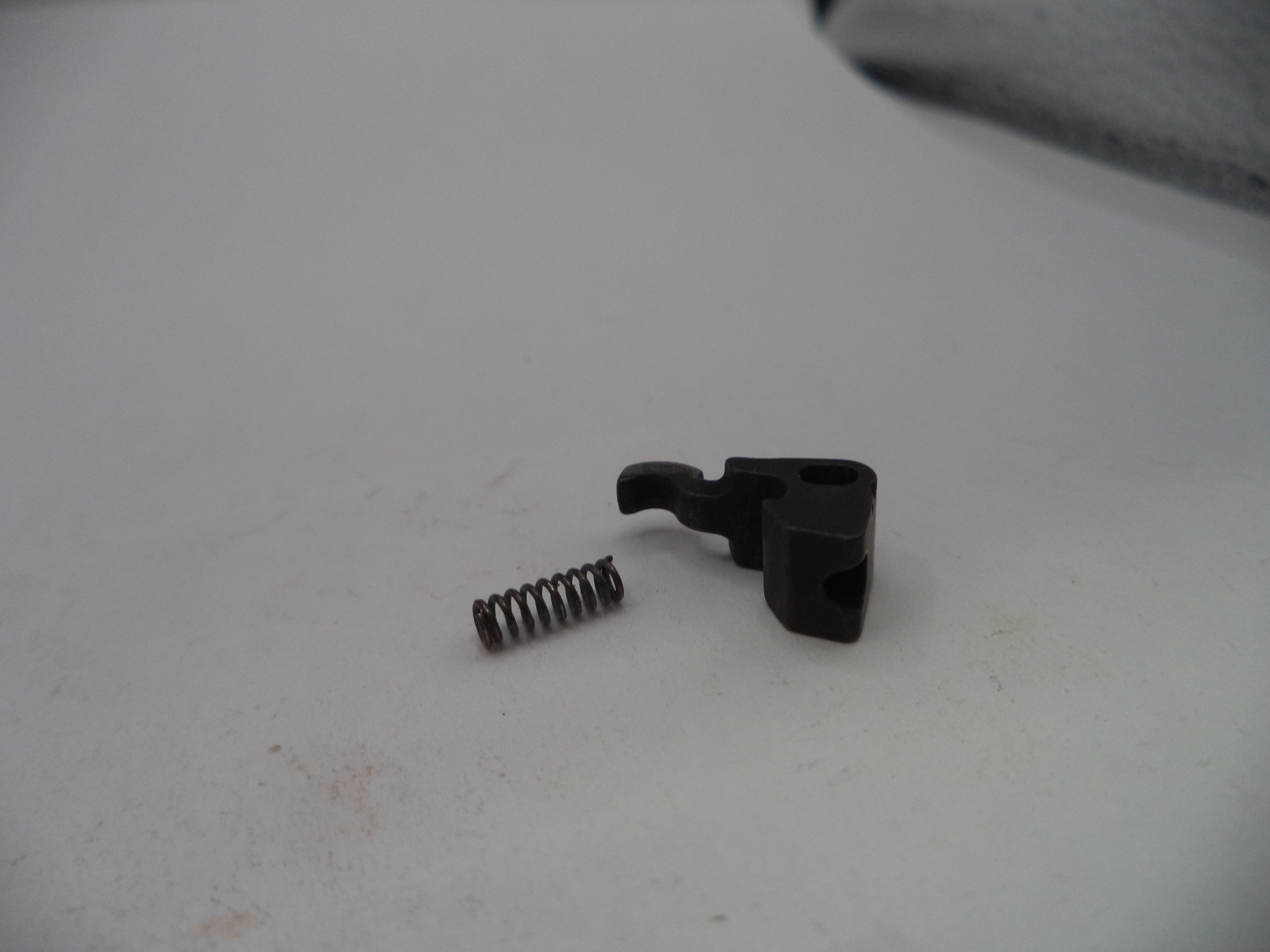A small black plastic mechanical switch component with a separate metal coil spring, placed on a light gray surface.
