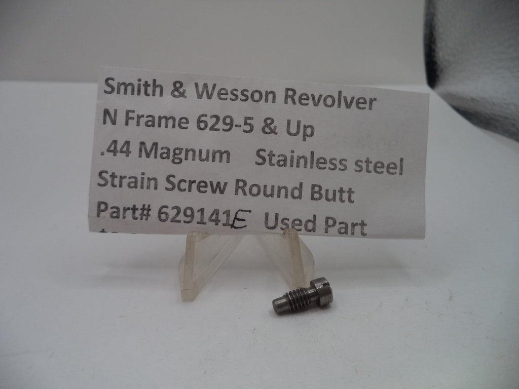 A small metal strain screw part displayed on a clear plastic stand with a handwritten label card that reads 'Smith & Wesson Revolver N Frame 629-5 & Up .44 Magnum Stainless steel Strain Screw Round Butt Part# 629141 Used Part'.