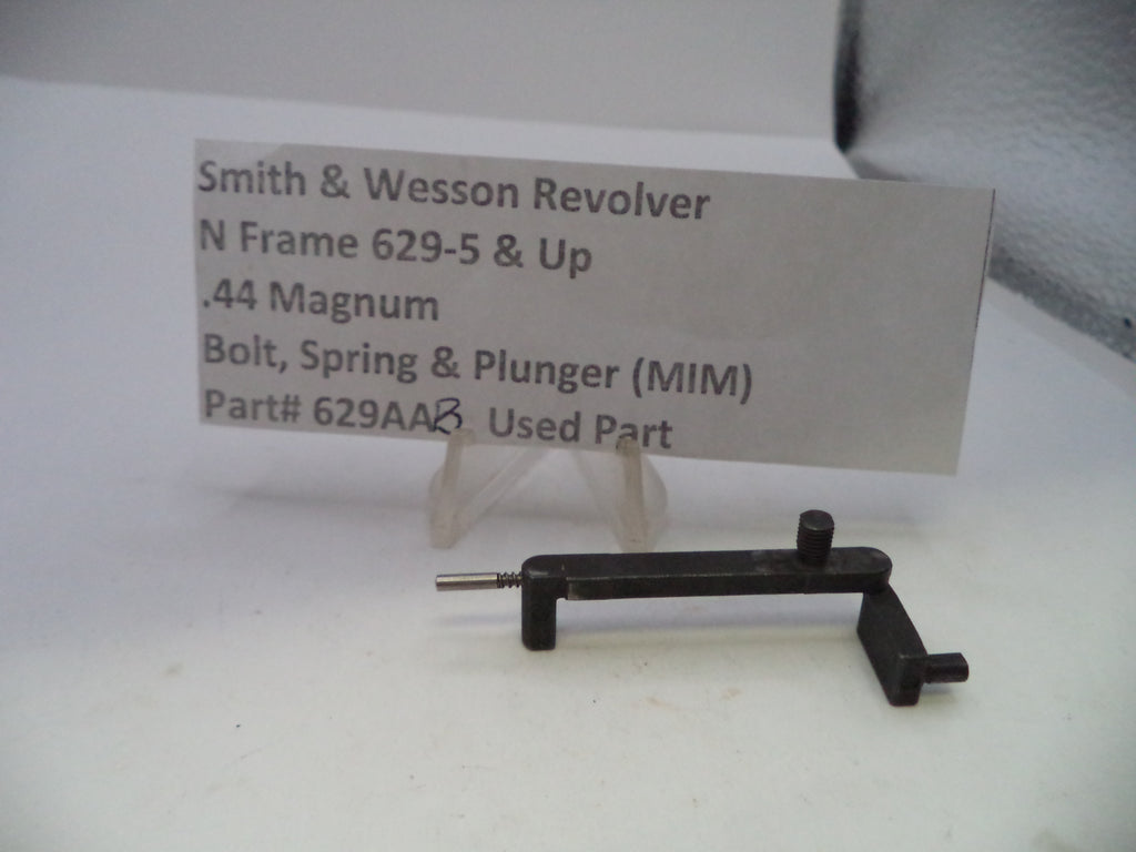 A used black metal Smith & Wesson revolver bolt, spring, and plunger part, displayed on a small clear stand in front of a paper label card.