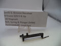 A used Smith & Wesson revolver bolt, spring, and plunger part shown on a white surface with a product information card behind it. The part is black metal with a small silver spring.