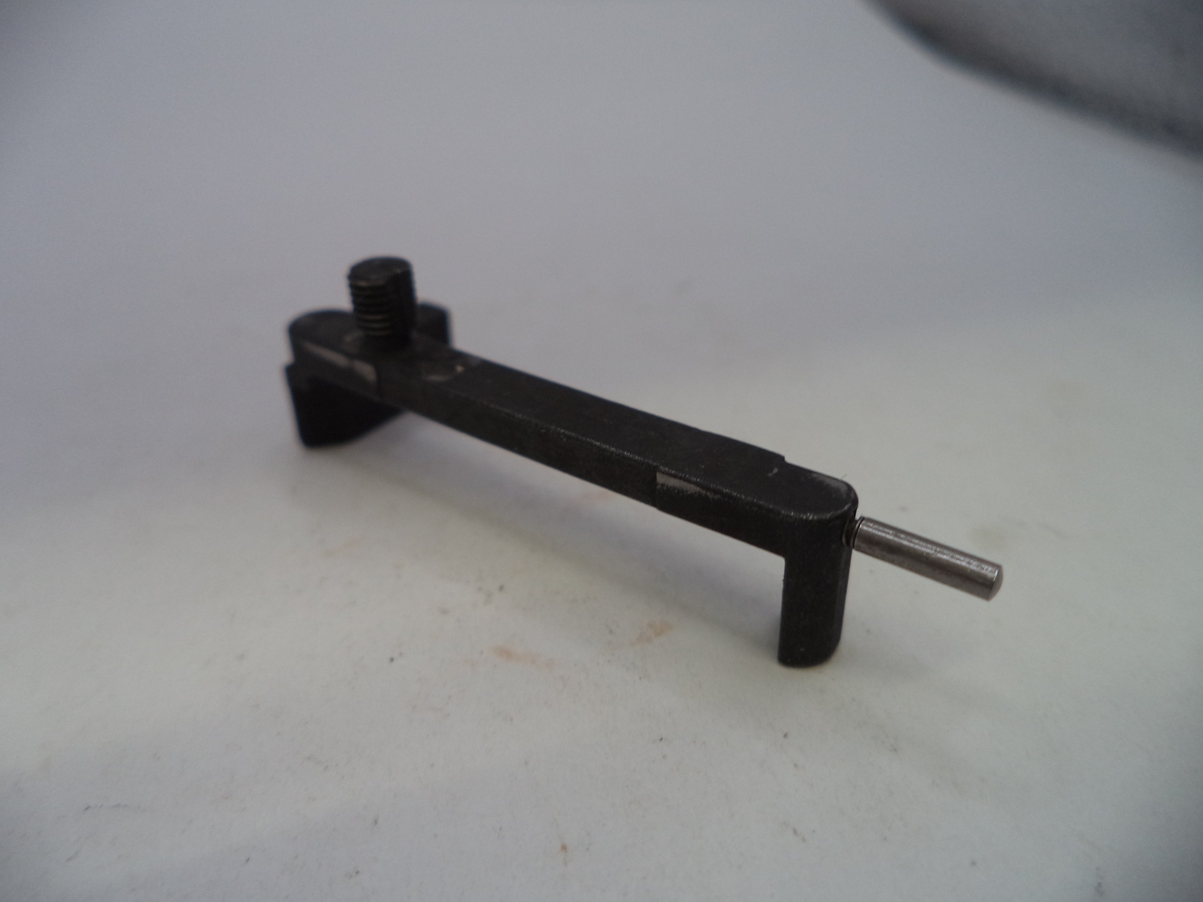 A small black metal tool or hardware piece with a threaded screw and a silver pin, photographed on a plain light background.