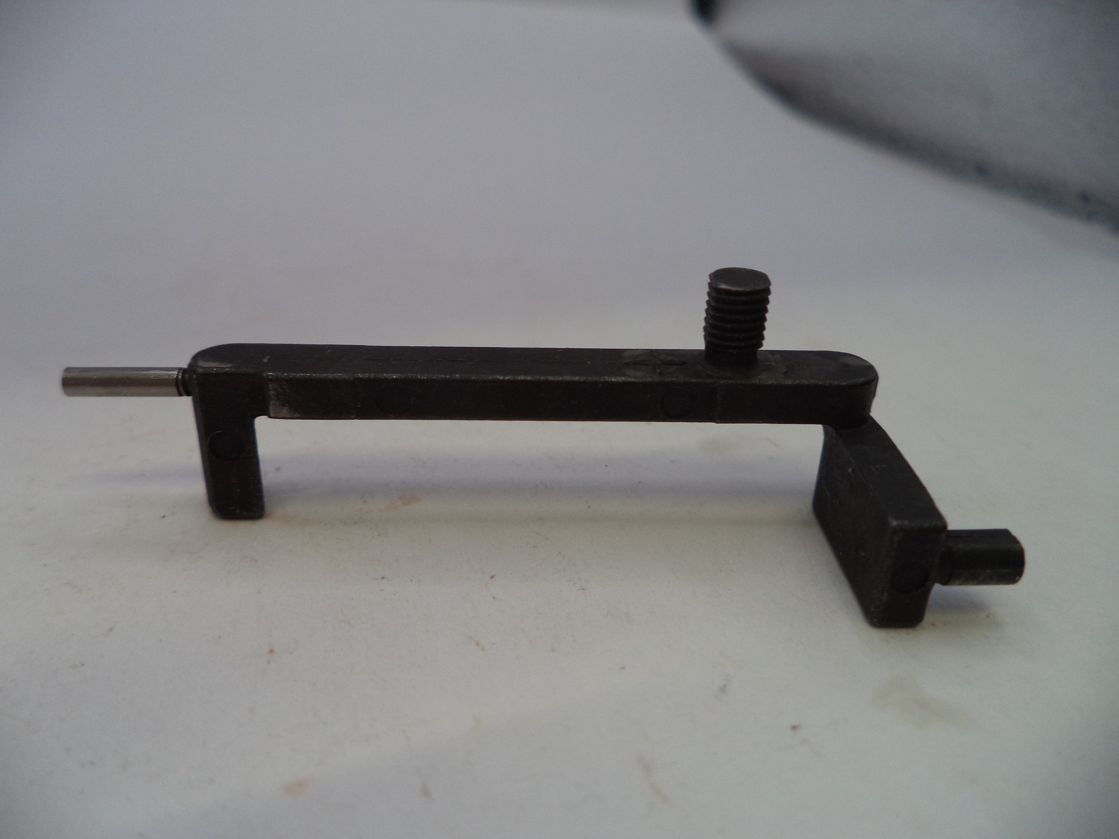 A black metal mechanical tool or fixture with a threaded screw post and a short protruding pin, photographed on a plain light background.