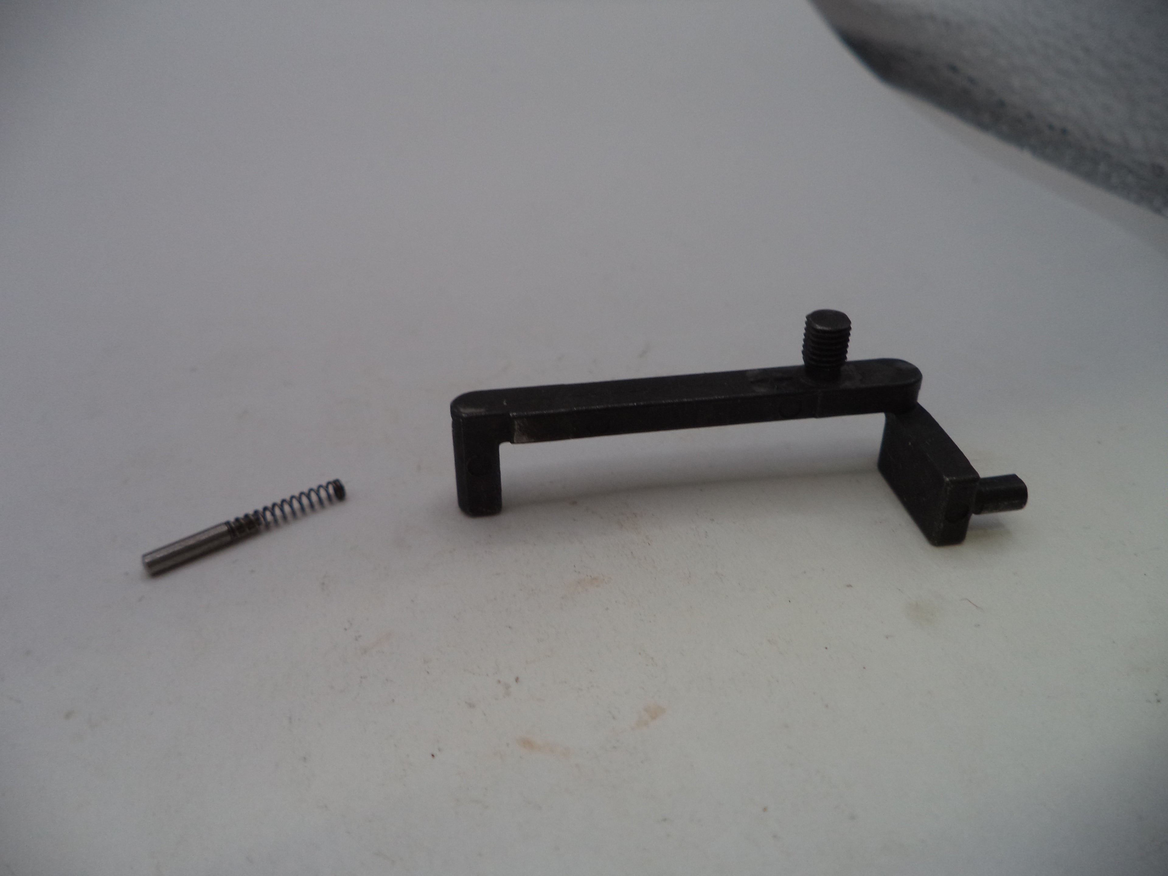 A black metal mechanical component with a small silver spring placed beside it on a light gray surface.