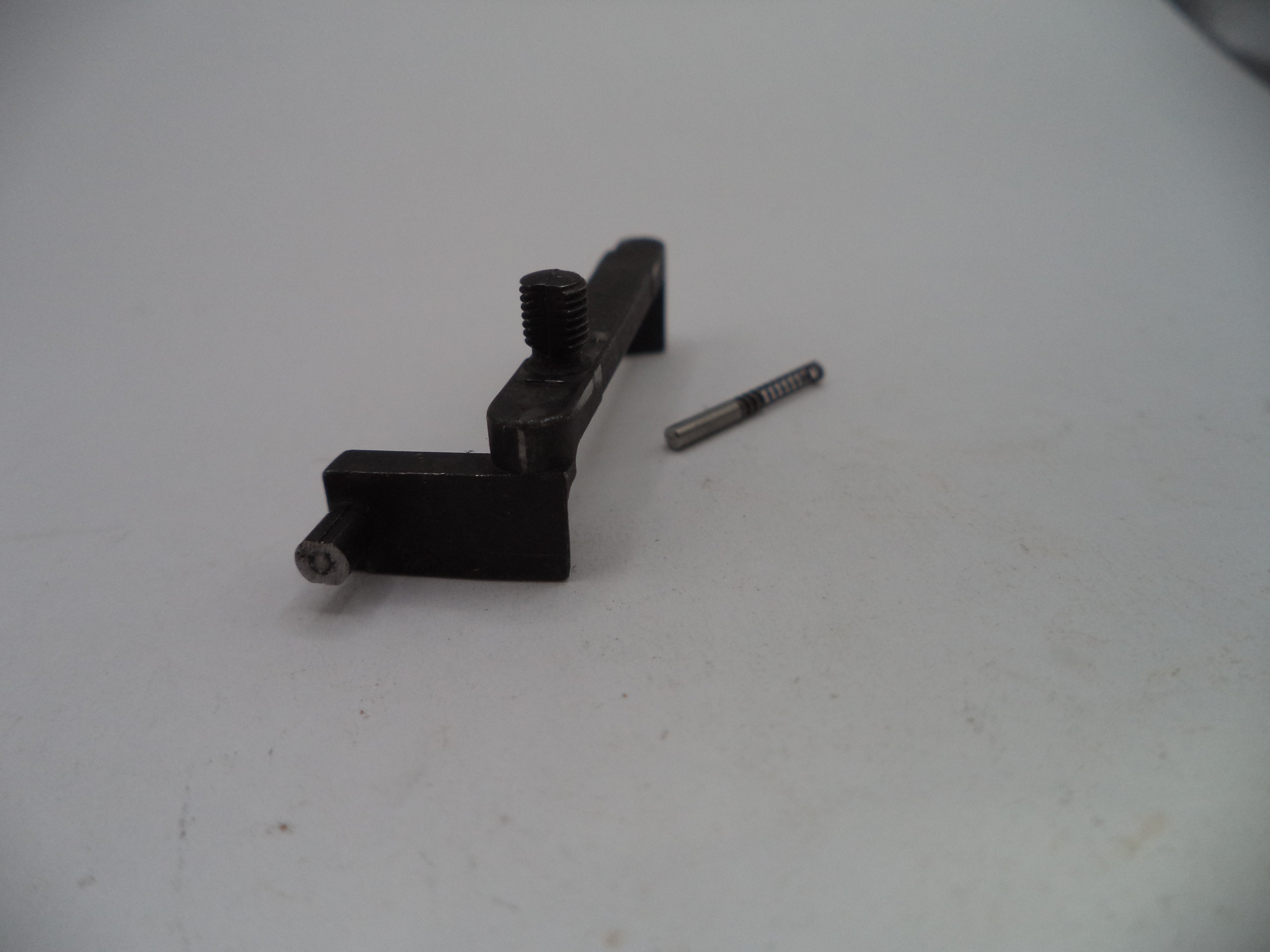 A small black metal mechanical component with a threaded screw post and a separate small silver screw, photographed on a plain light gray surface.