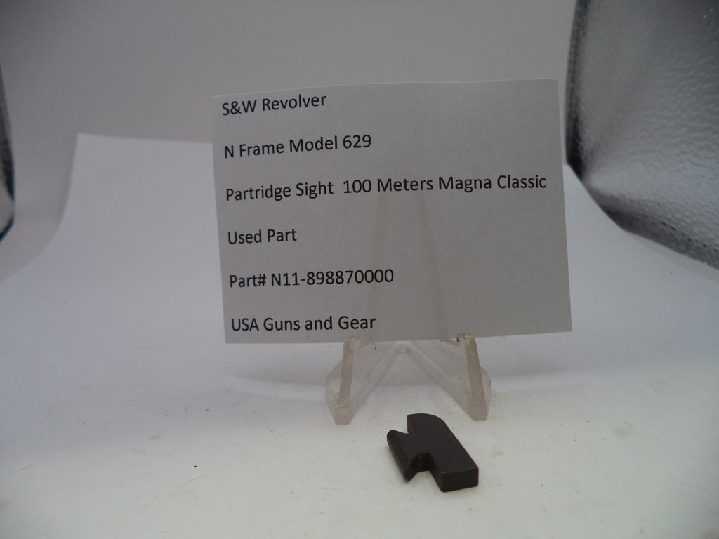 A small black metal revolver part displayed on a clear acrylic stand in front of a white paper label card. The label reads 'S&W Revolver N Frame Model 629 Partridge Sight 100 Meters Magna Classic Used Part' with part number 'N11-898870000' and 'USA Guns and Gear' at the bottom.