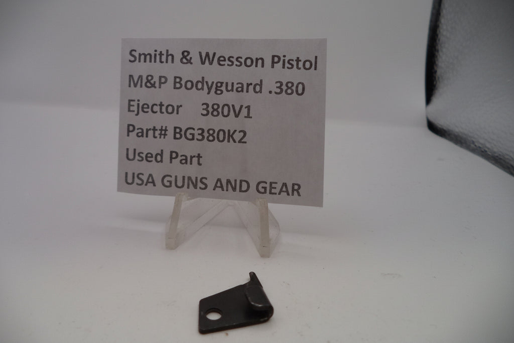 Black ejection part for Smith & Wesson pistol on a white background with a label.