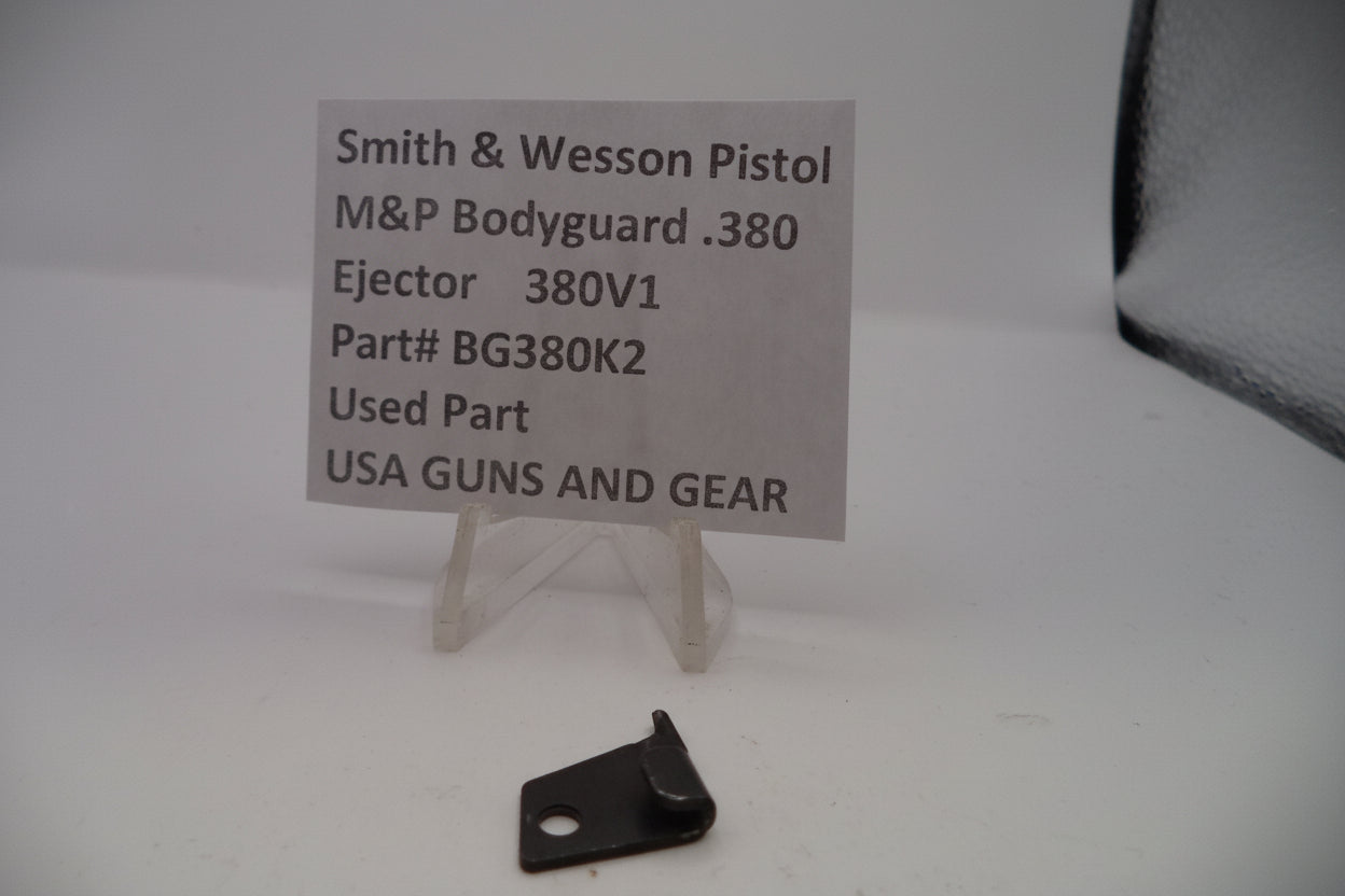 Black ejection part for Smith & Wesson pistol on a white background with a label.