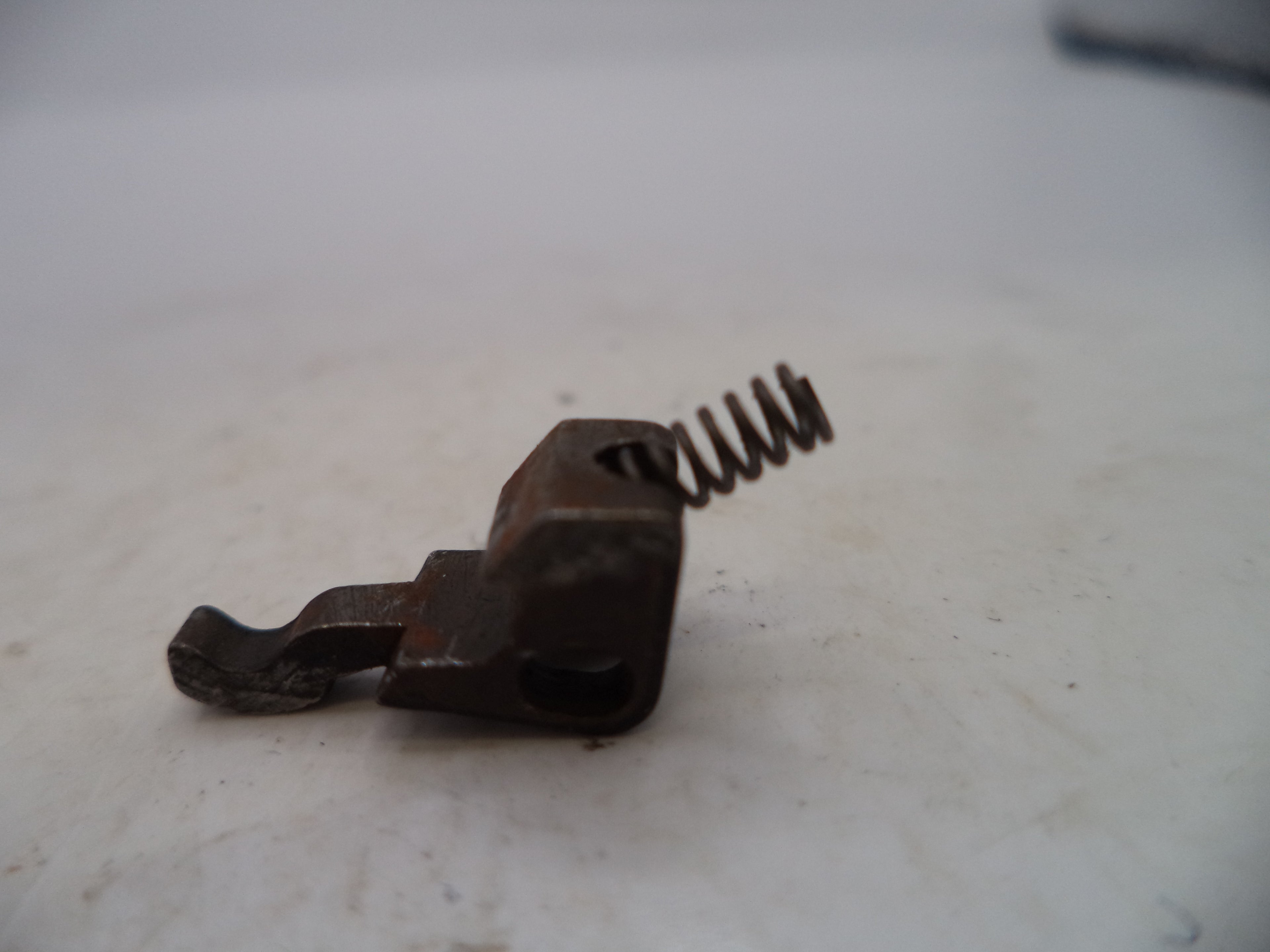 Rust-colored metal component with a spring on a light background