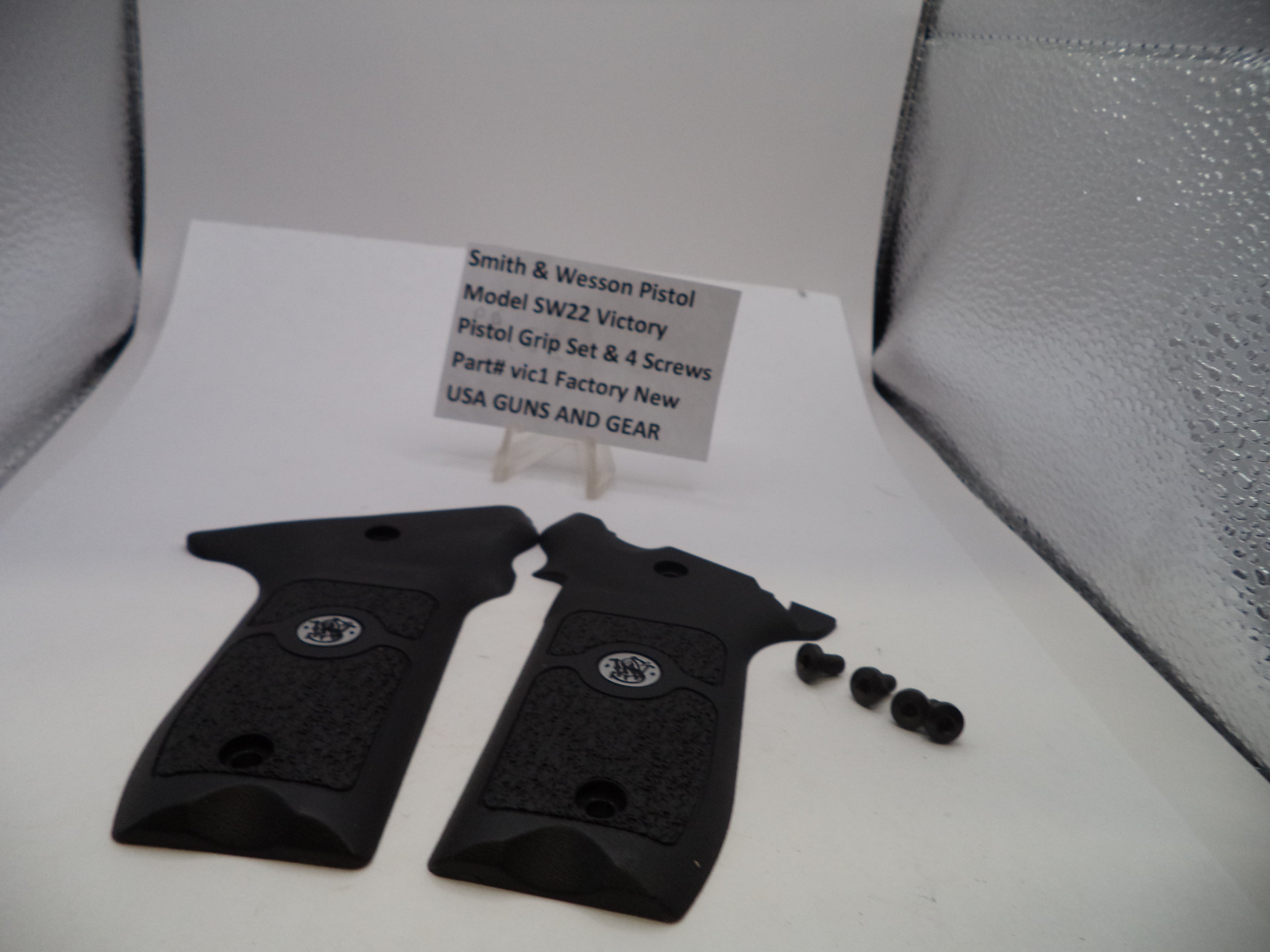 Black pistol grips with screws on a white surface, accompanied by a sign detailing product information.