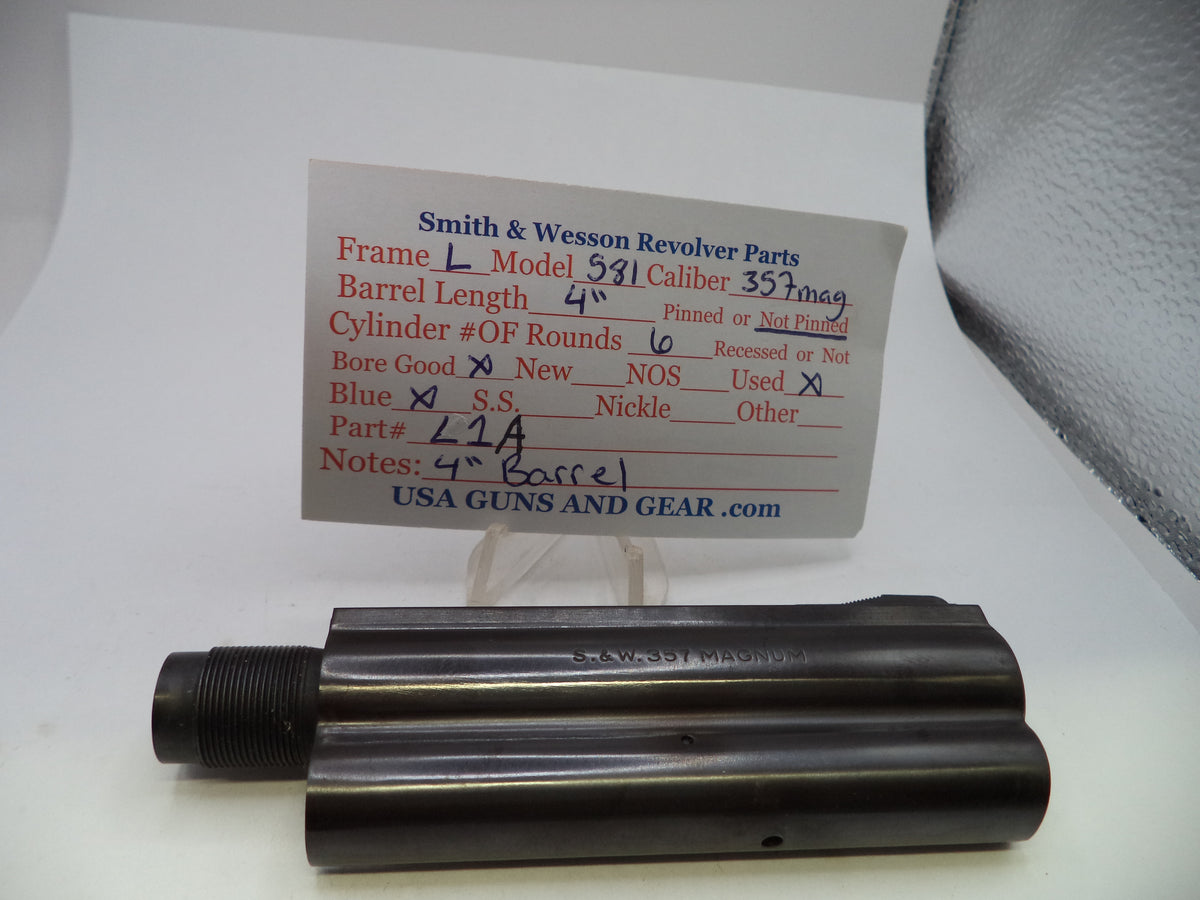 A pair of dark metal Smith & Wesson revolver barrel components displayed on a white surface with a handwritten parts identification card behind them.