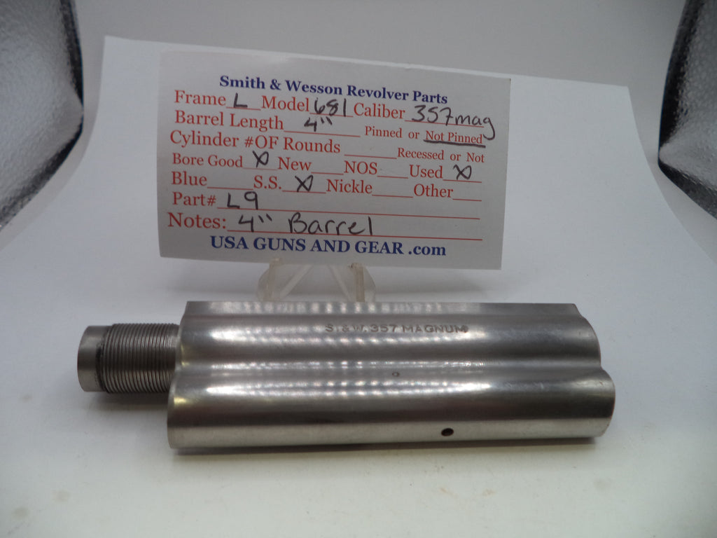 A metal cylindrical gun part with a threaded male end, shown on a white surface with a handwritten paper label card behind it reading Smith & Wesson Revolver Parts.