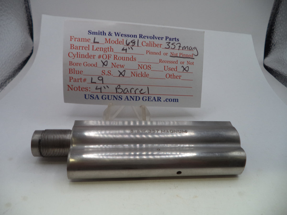 A metal cylindrical gun part with a threaded male end, shown on a white surface with a handwritten paper label card behind it reading Smith & Wesson Revolver Parts.