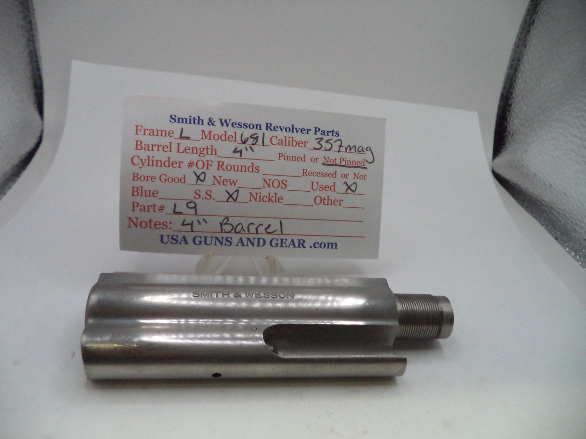 A metal revolver barrel spacer or barrel section part displayed on a white surface with a handwritten parts identification card behind it. The card shows Smith & Wesson revolver parts details including barrel length and notes.