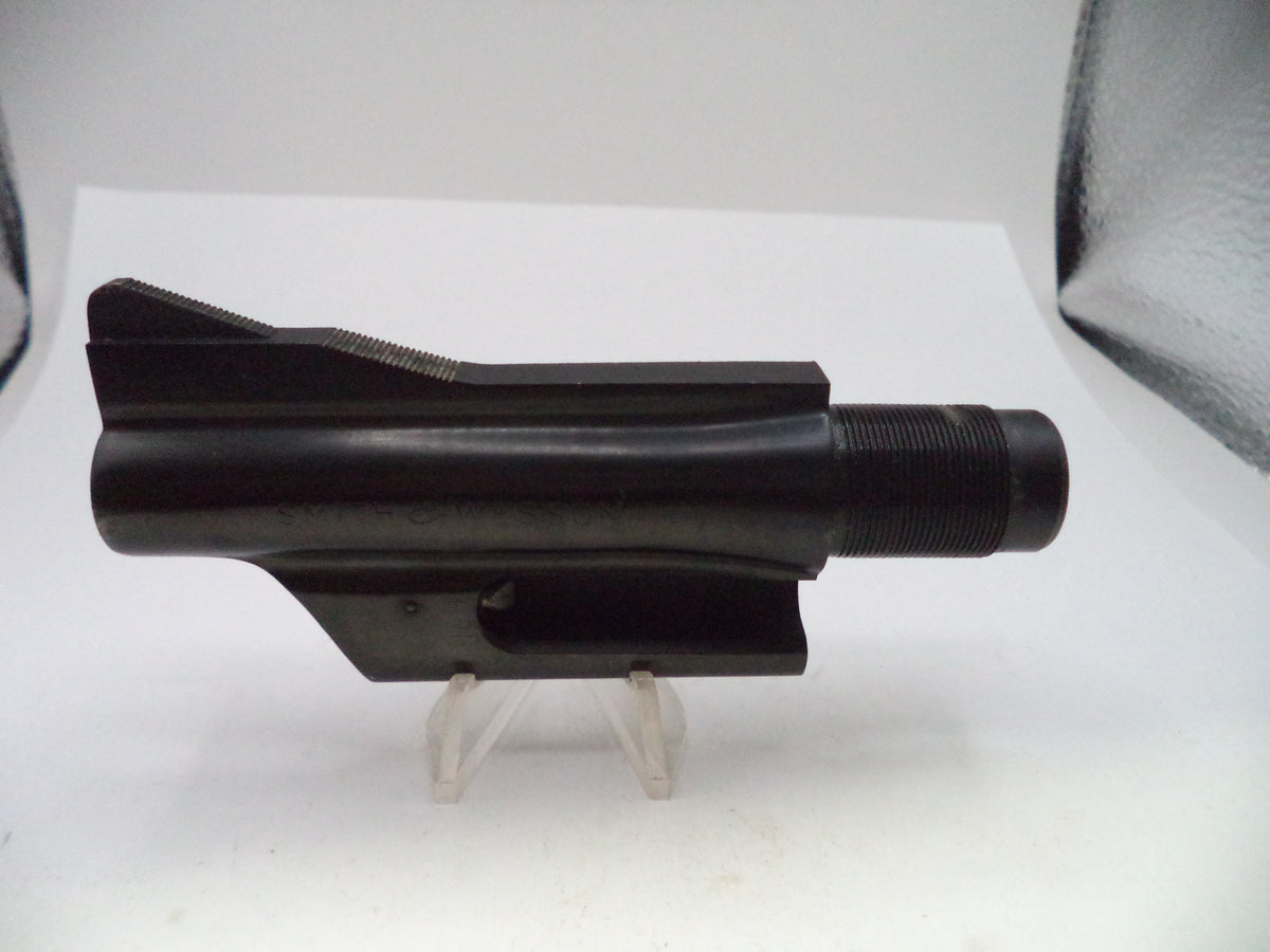 A black metal firearm barrel shroud or receiver component displayed on a small clear stand against a white background.