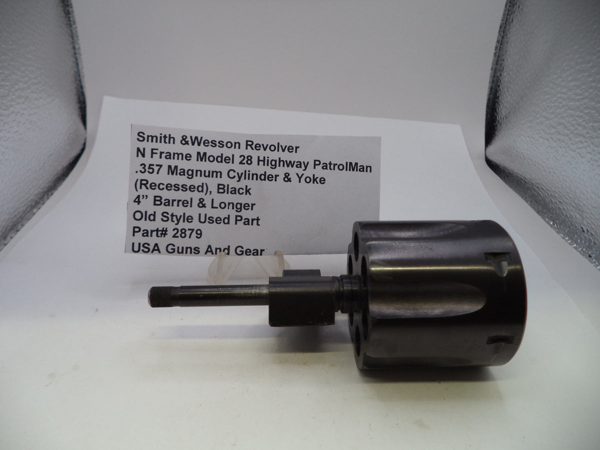 A used black Smith & Wesson revolver cylinder and yoke part with a short barrel, placed on a white surface in front of a handwritten product information card.