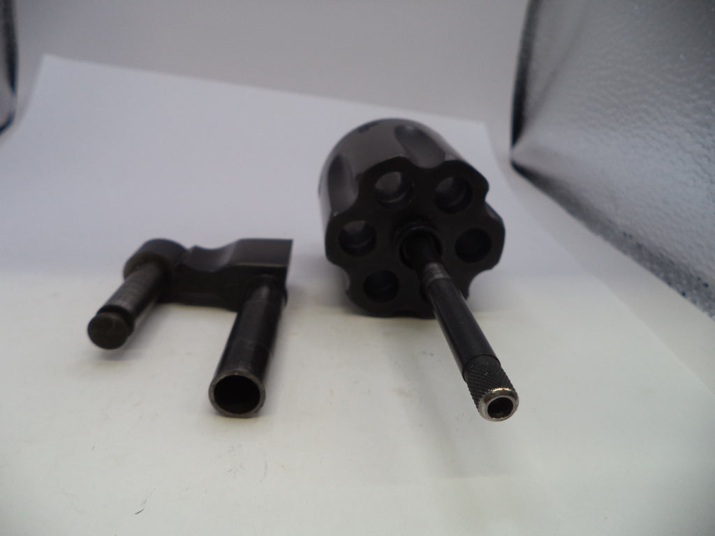 A black metal revolver-style accessory or component set photographed on a white surface, with two separate pieces placed beside a larger cylindrical piece with multiple circular openings and a long protruding rod.