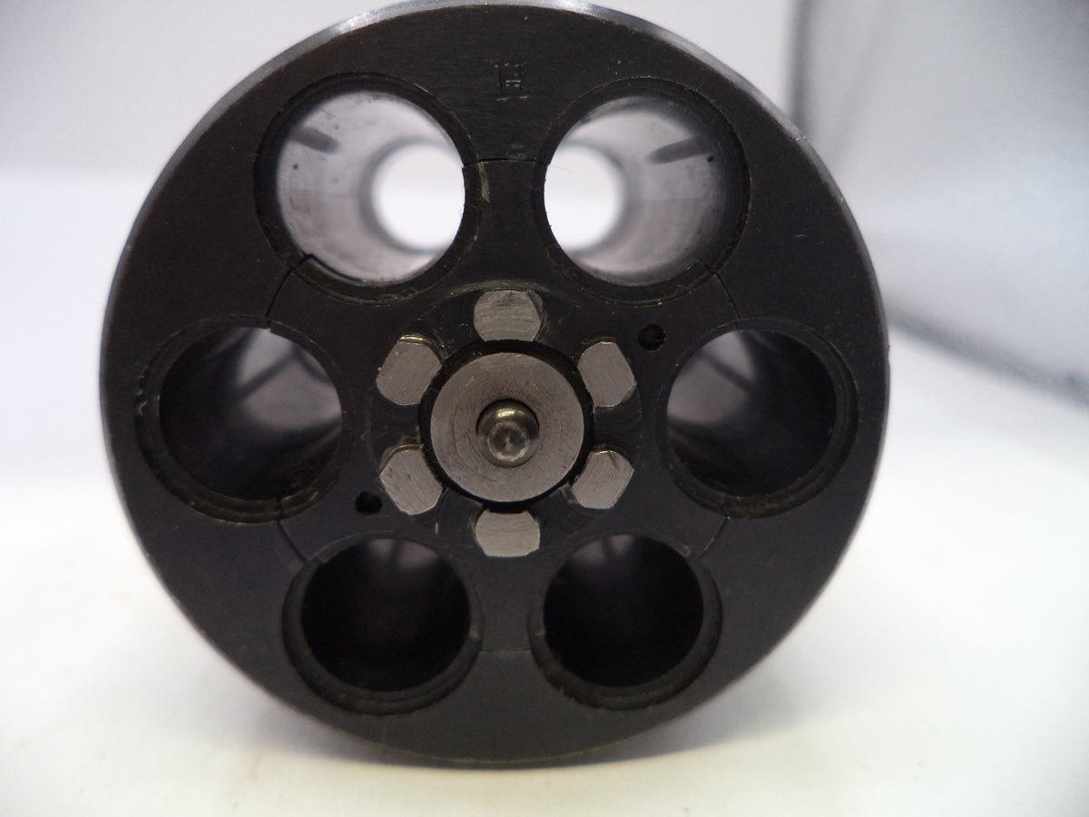 A close-up of a black circular mechanical component with six circular openings and a central metallic screw fastener, photographed on a white background.