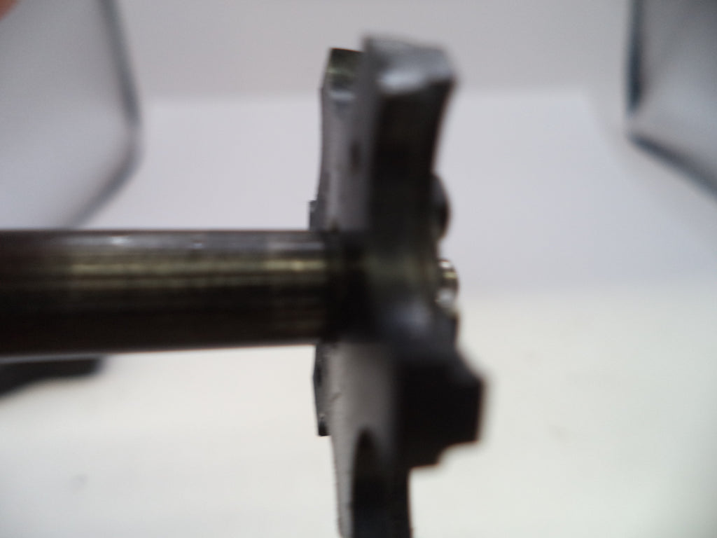 A close-up, blurry shot of a dark metal mechanical component or shaft assembly against a white background.