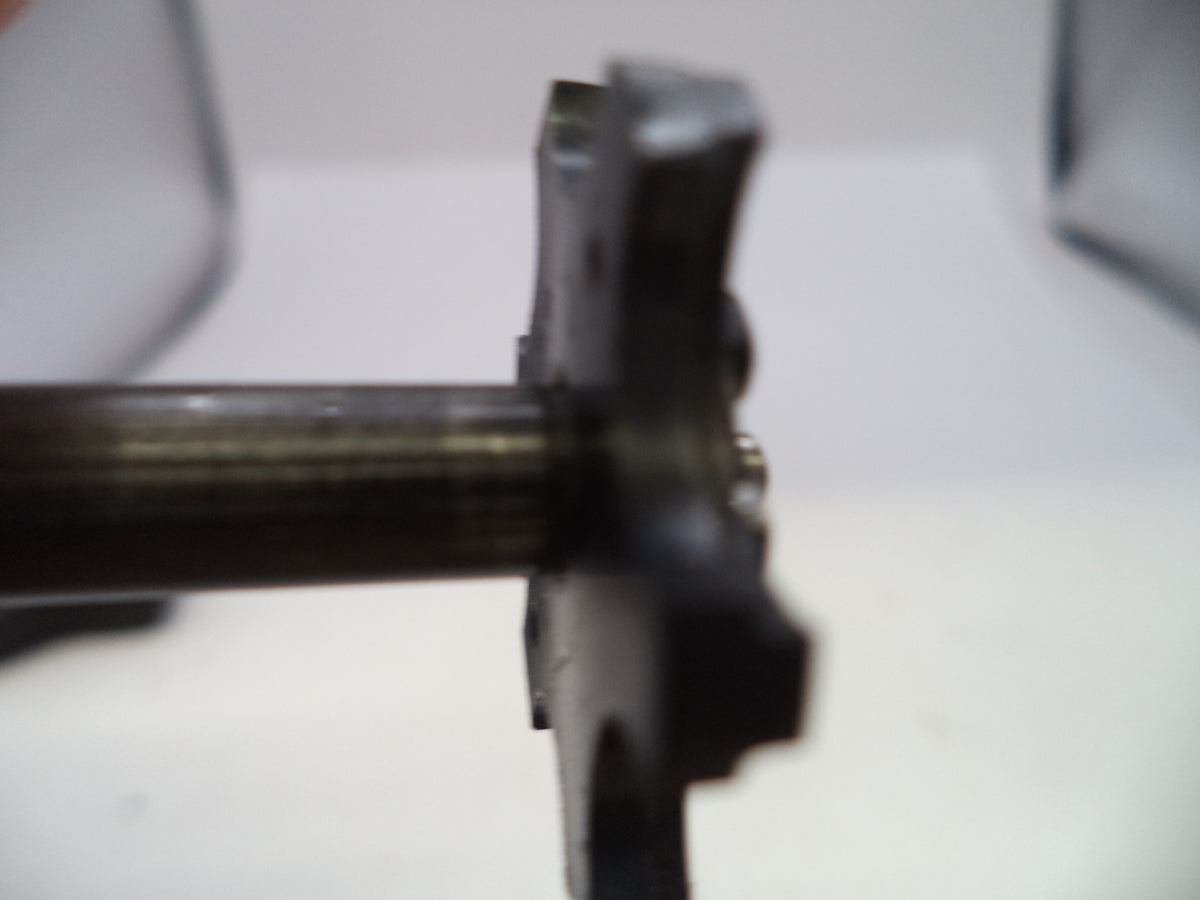 A close-up, blurry shot of a dark metal mechanical component or shaft assembly against a white background.