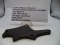A black metal side plate for a Smith & Wesson revolver, displayed on a clear plastic stand with an identification card in the background.