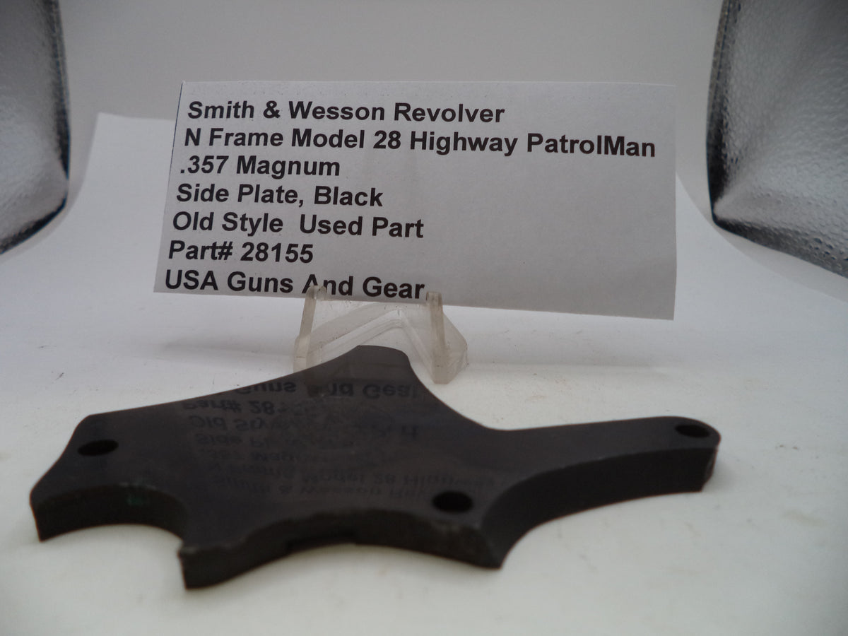 A black metal side plate for a Smith & Wesson revolver, displayed on a clear plastic stand with an identification card in the background.