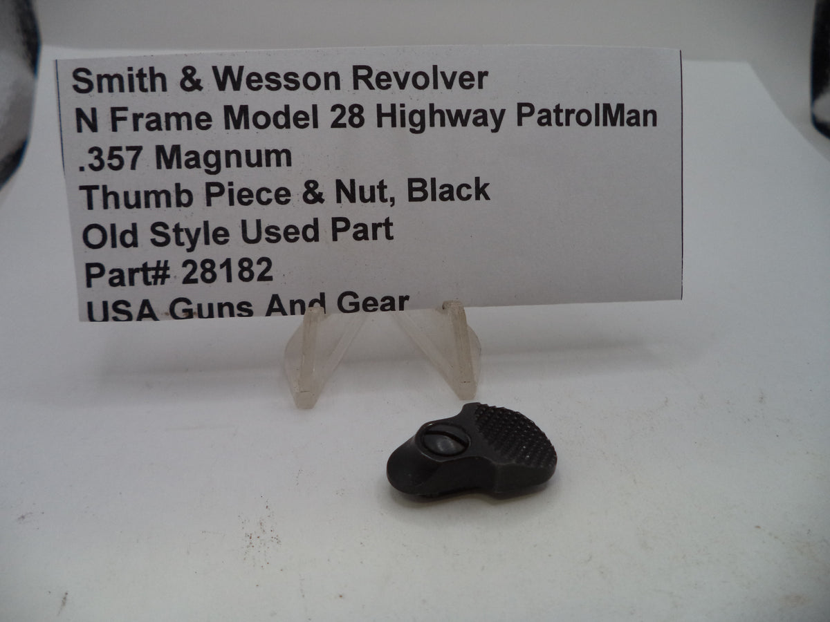 A black used thumb piece and nut part for a Smith & Wesson revolver, displayed on a clear plastic stand in front of a white paper label card.