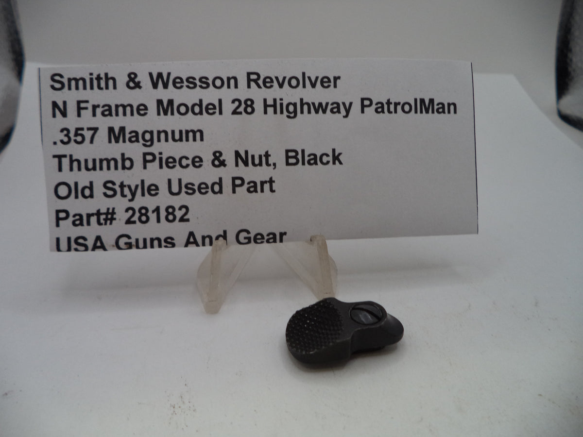 A black used thumb piece and nut part for a Smith & Wesson revolver, displayed on a clear plastic stand next to a white label card with product details.