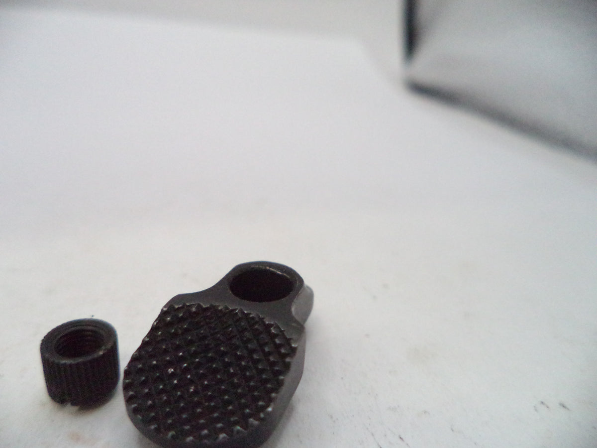 A close-up of a small black textured metal knob or toggle piece next to a matching threaded cap on a white surface.