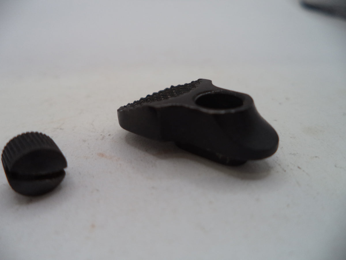 A close-up of a black metal adjustment knob or hardware component with a textured ridged top and a separate matching cap placed beside it on a light gray surface.