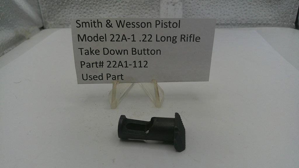 Smith & Wesson pistol take down button part on a white surface with a label.