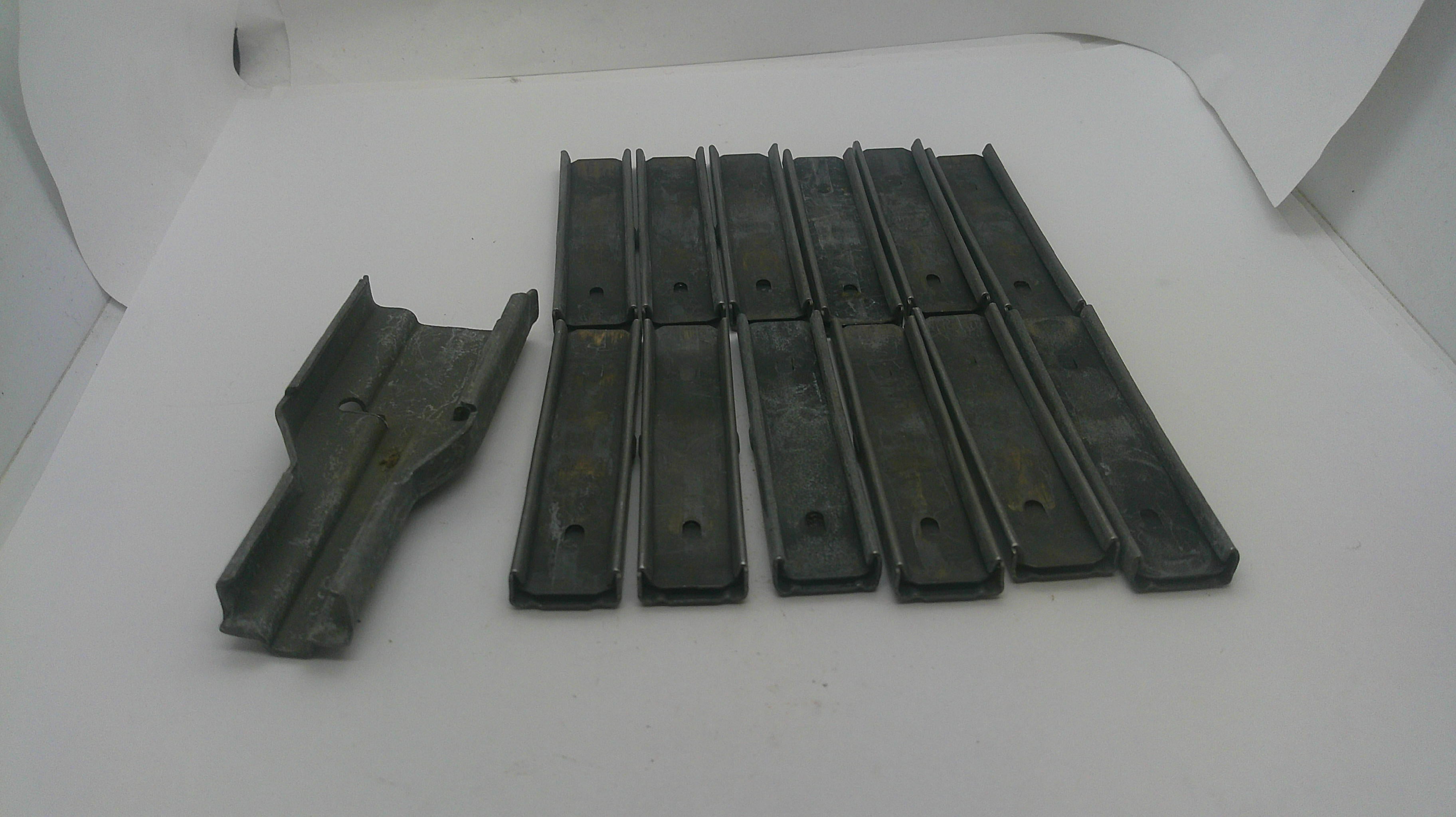A set of dark gray metal or plastic replacement parts, including one larger piece on the left and several long narrow strips on the right, displayed on a white background.