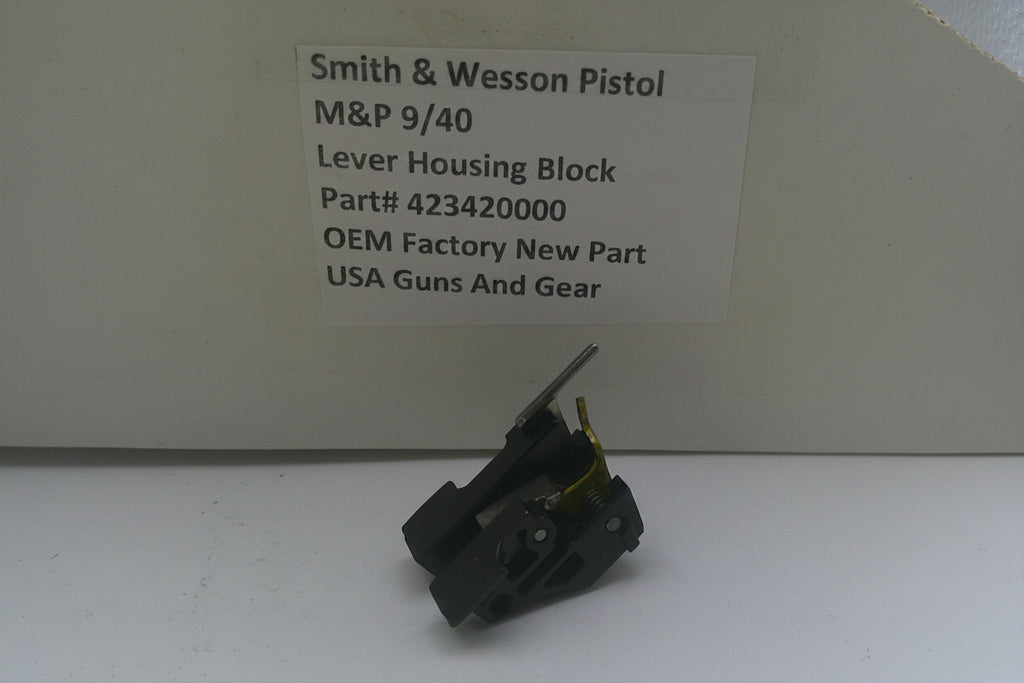 A small black metal lever housing block part for a Smith & Wesson pistol, displayed in front of its branded cardboard packaging box with a white label.