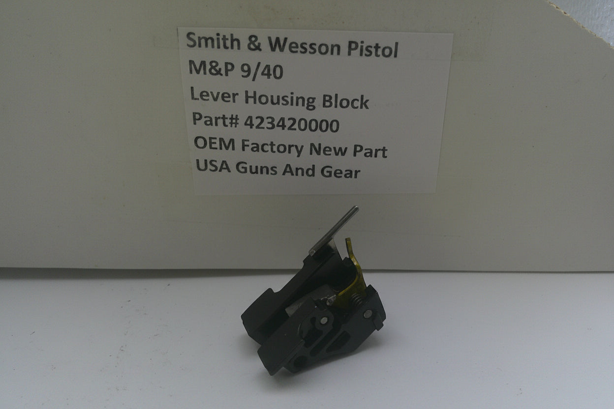 A small black metal lever housing block part for a Smith & Wesson pistol, displayed in front of its branded cardboard packaging box with a white label.