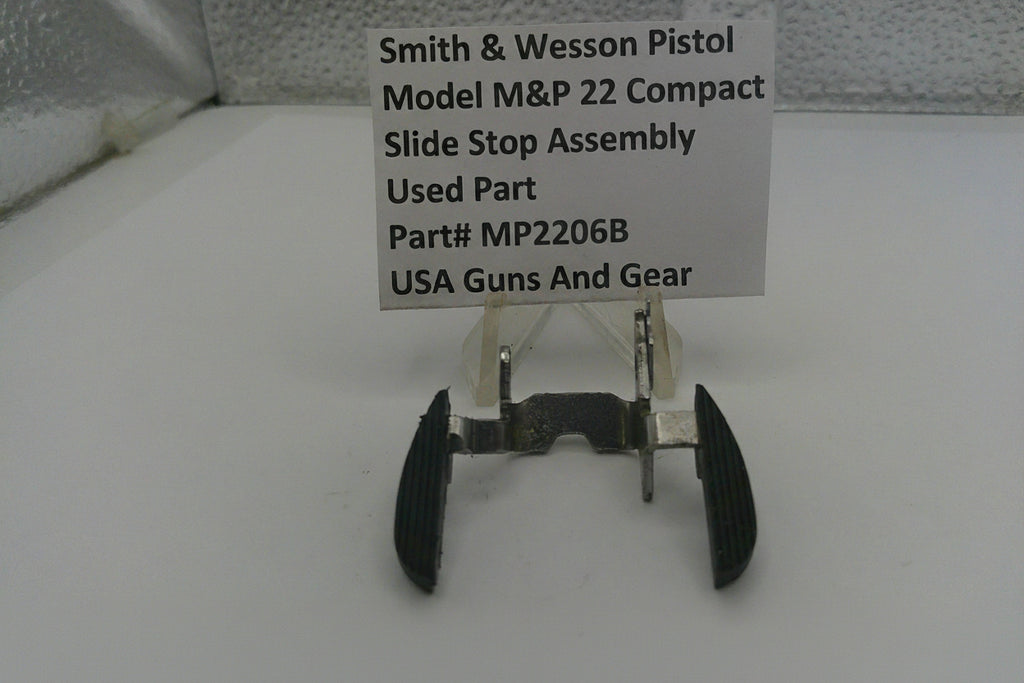 Smith & Wesson pistol slide stop assembly on a white surface with a label.
