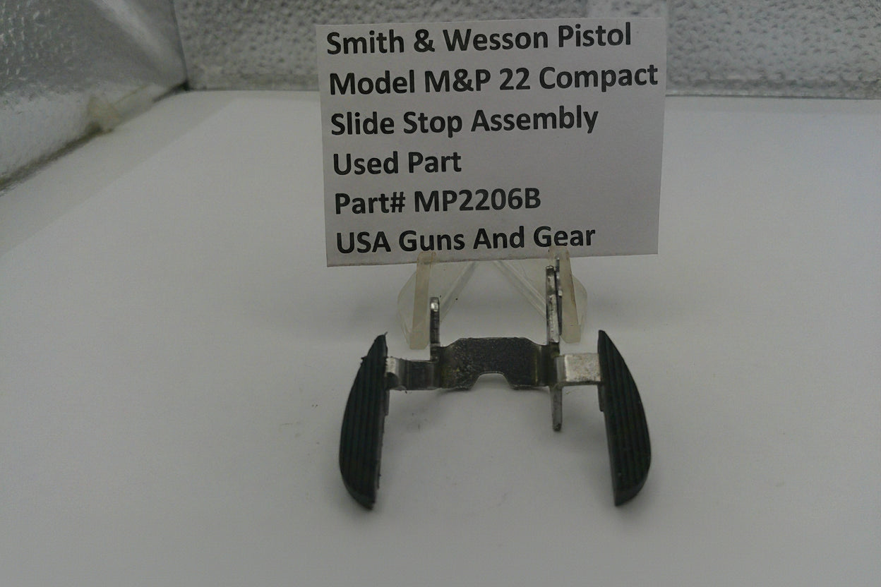 Smith & Wesson pistol slide stop assembly on a white surface with a label.