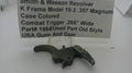 A used metal Smith & Wesson revolver trigger part, model 19-3 .357 Magnum, shown on a white surface with a handwritten paper label in the background.