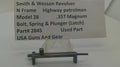 A used metal latch part for a Smith & Wesson revolver, displayed on a clear stand with a paper label card in the background. The label details the part number 2845 and notes it is a used part for a Model 28 .