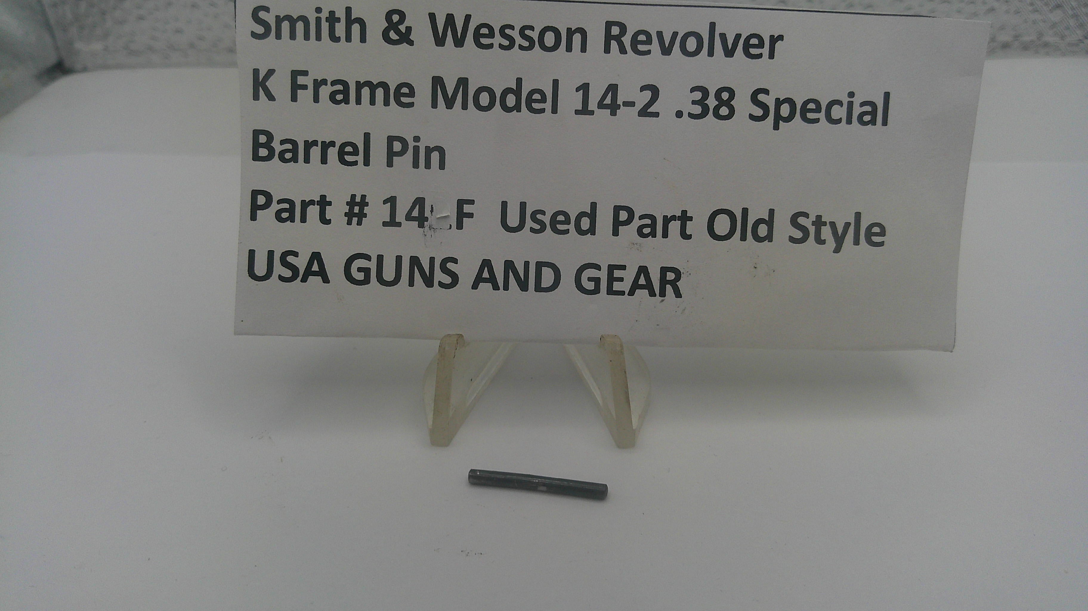 A small dark metal barrel pin displayed on a white stand in front of a white sign that reads 'Smith & Wesson Revolver K Frame Model 14-2 .38 Special Barrel Pin Part # 14-F Used Part Old Style USA GUNS AND GEAR'.
