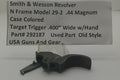 A used Smith & Wesson revolver trigger part, specifically a Model 29-2 .44 Magnum case colored target trigger, displayed on a clear stand in front of a white paper label with product details.