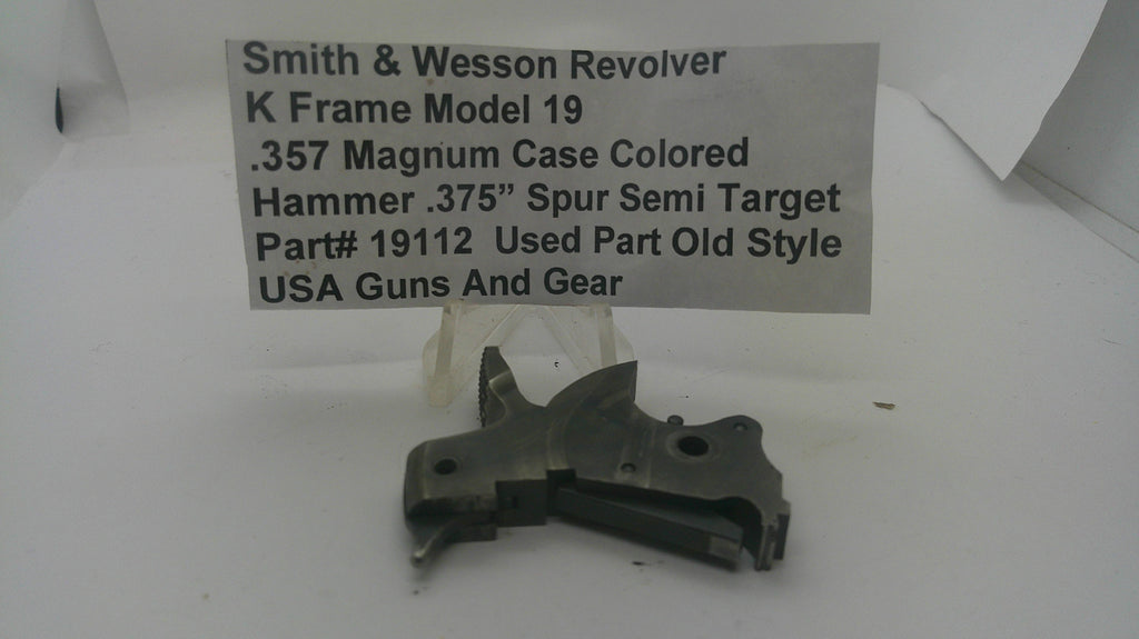A used metal firearm part, identified as a Smith & Wesson revolver hammer, displayed on a white surface with a text label card in the background.