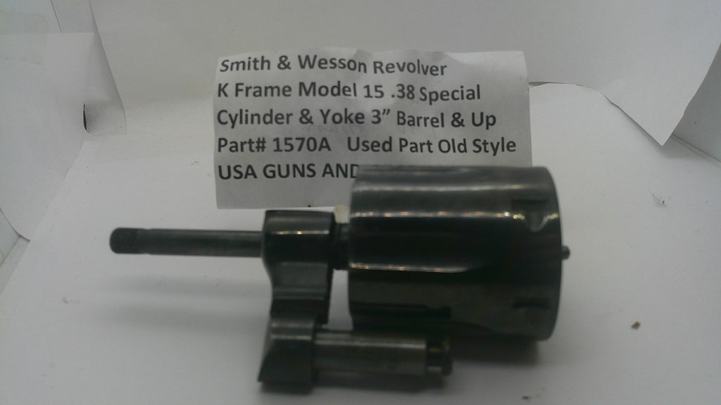 A used black metal Smith & Wesson revolver cylinder and yoke part, shown on a white background with a handwritten paper label behind it.
