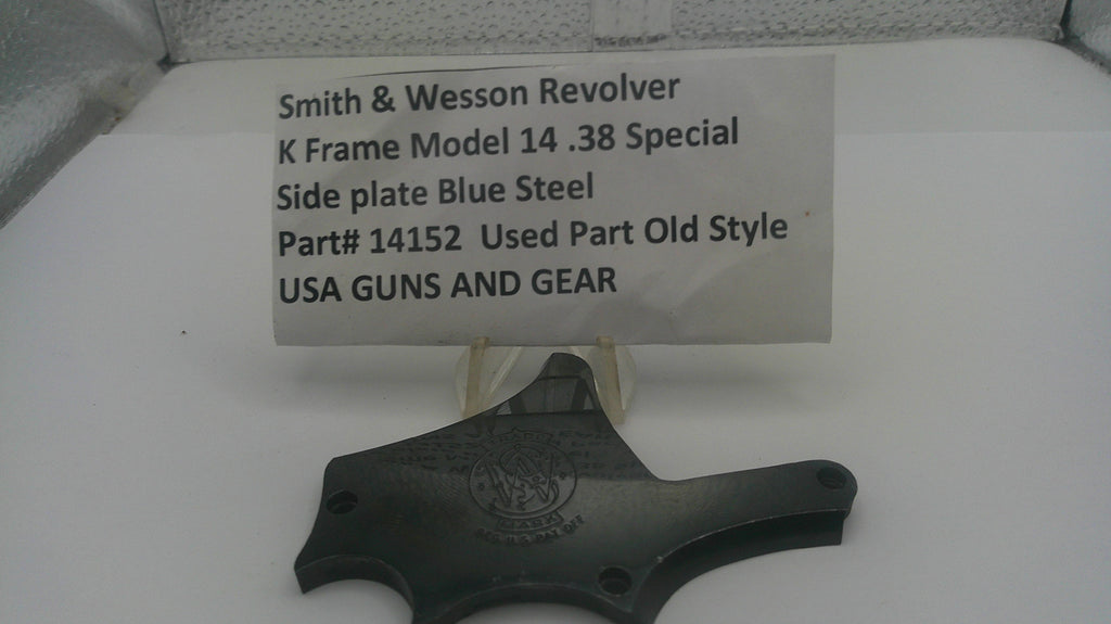 A used black steel side plate for a Smith & Wesson revolver, displayed on a white surface with a white label card showing the part number and model details.