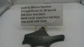 A used black steel side plate for a Smith & Wesson revolver, displayed on a white surface with a white label card showing the part number and model details.