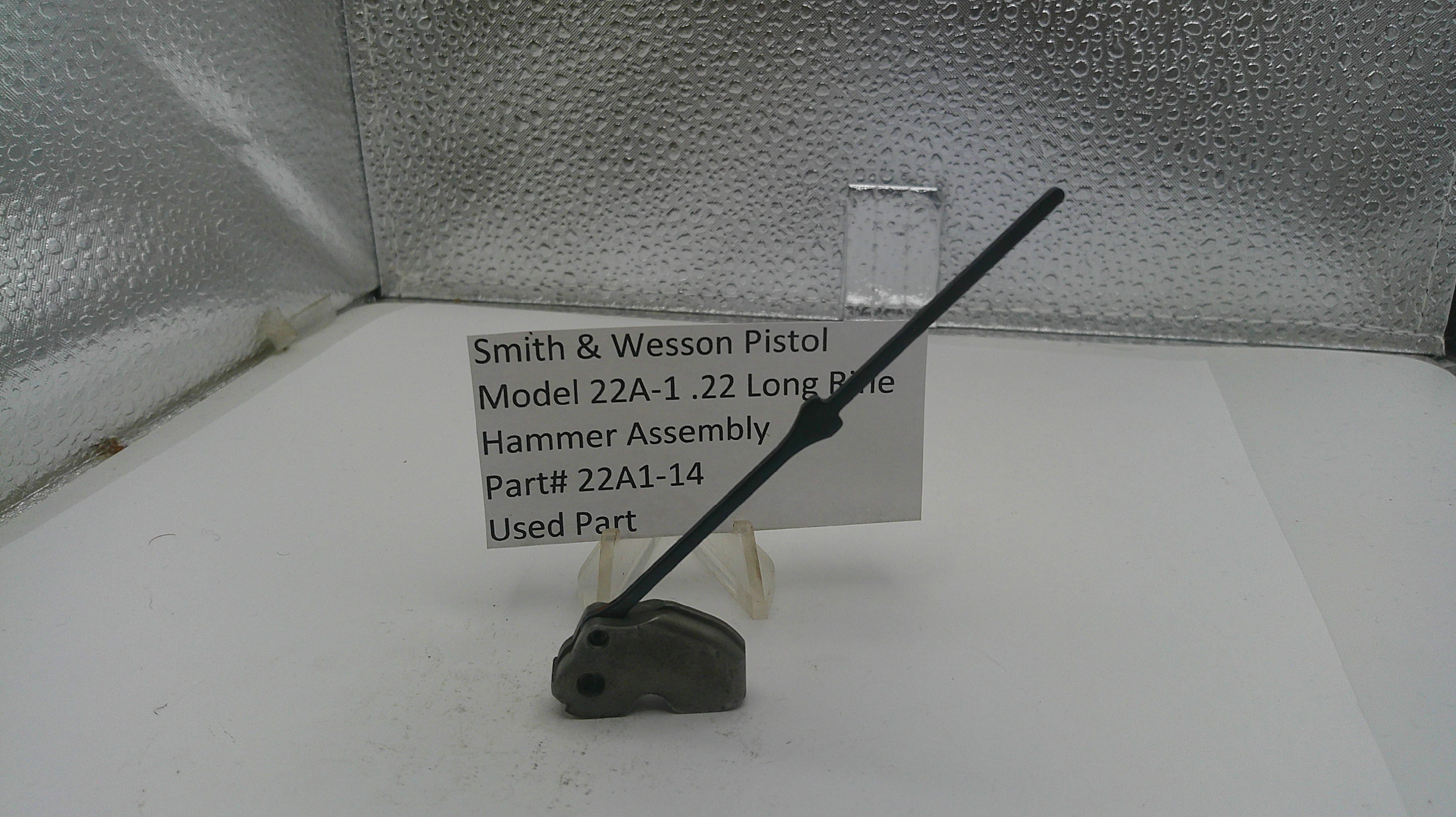 Smith & Wesson pistol hammer assembly on a white surface with a label.