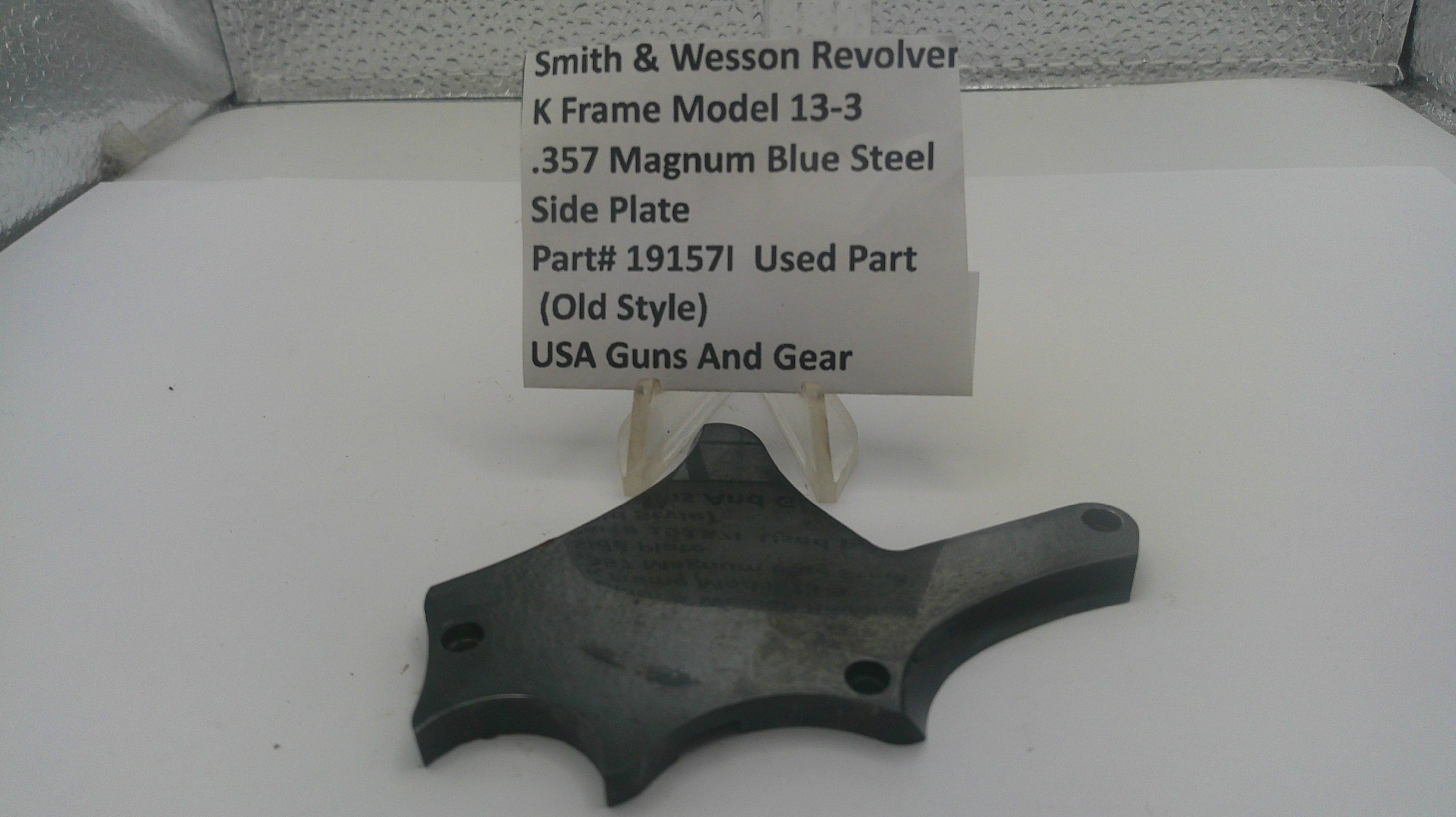 A used black metal Smith & Wesson revolver side plate part, displayed on a clear plastic stand with a white label card identifying the part number and manufacturer.
