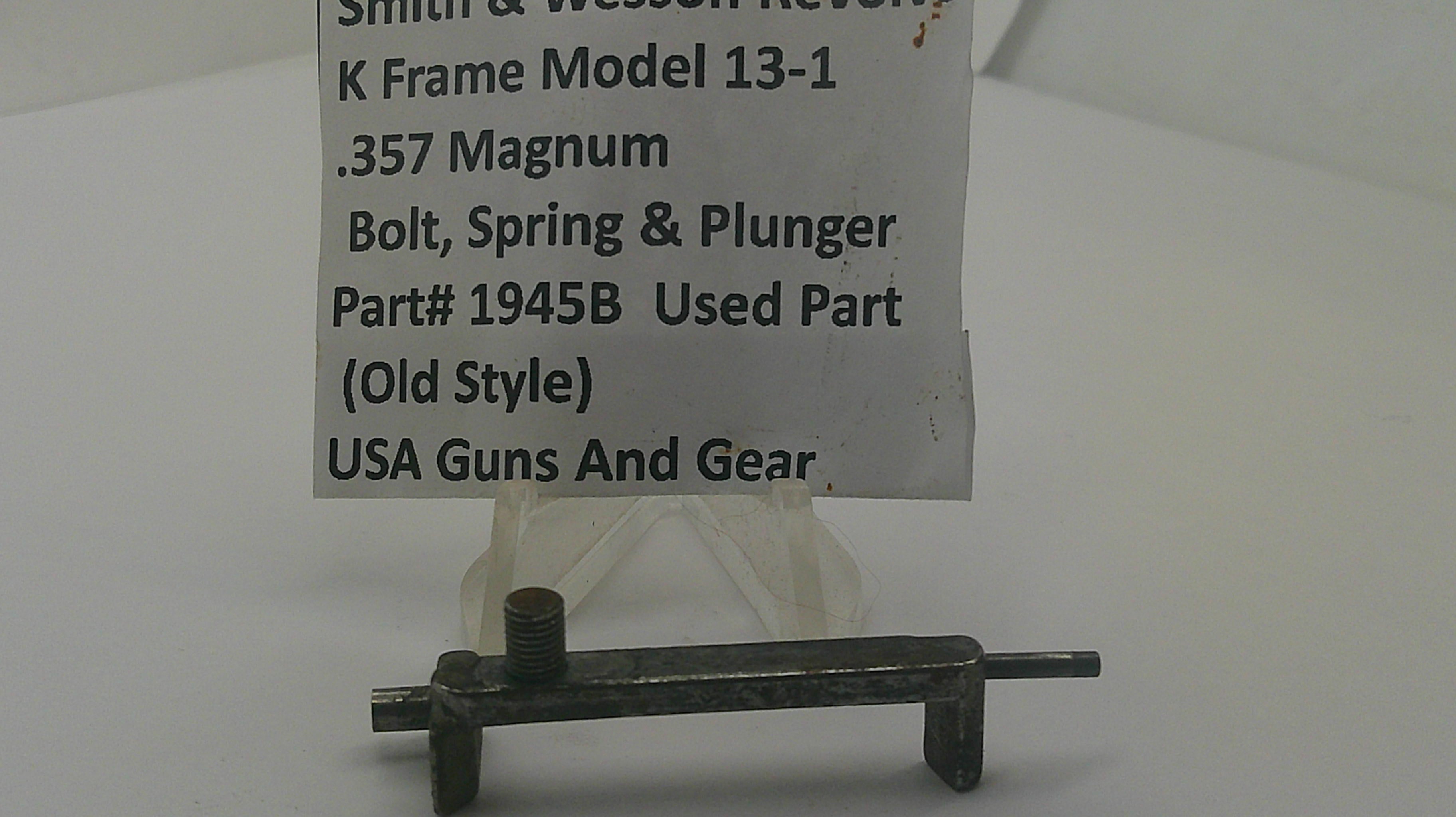 A small used metal part, identified as a bolt, spring, and plunger for a K frame model, displayed on a clear stand with a paper label card. The label reads 'Smith & Wesson Review K Frame Model 13-1 .